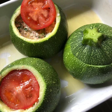 Runde Zucchini mit Füllung und Tomatenscheiben in einer Form.