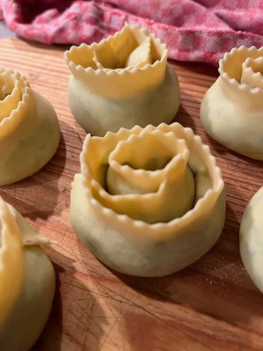 Ungekochte gefüllte Pasta in Rosenform auf einem Holzbrett.